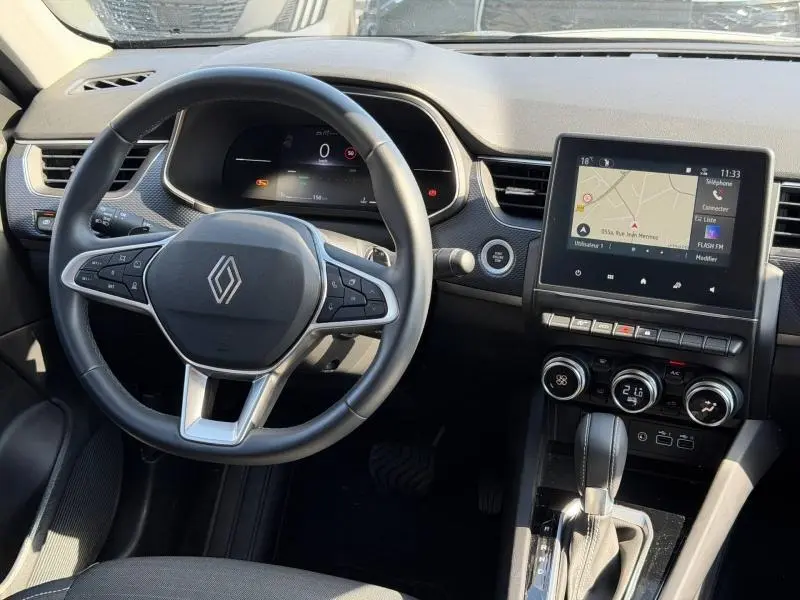 Vue intérieure du tableau de bord et volant du Renault Arkana 2025 gris métallique, avec écran tactile et commandes au volant.