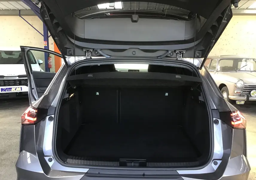 Vue arrière du coffre ouvert du Renault Symbioz gris Cassiopée, mettant en valeur l'espace de chargement et les feux arrière allumés.