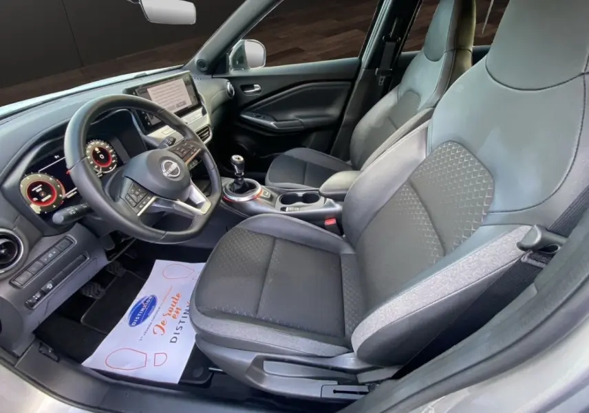 Vue intérieure côté conducteur du Nissan Juke gris clair 2025, montrant sièges tissu et cuir, volant multifonctions et écran tactile.