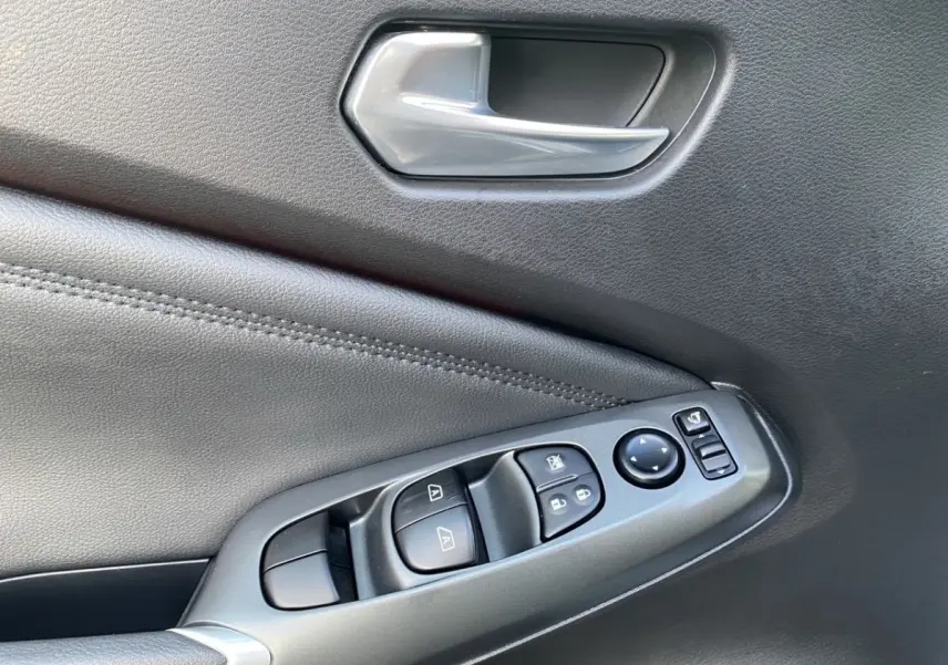 Gros plan sur la commande de lève-vitres et rétroviseurs côté conducteur, garniture intérieure noire du Nissan Juke 2025.