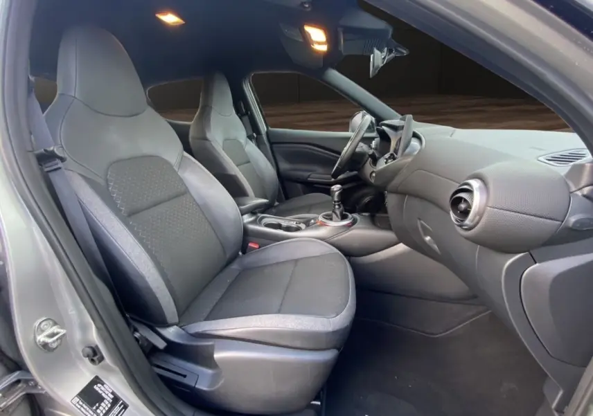 Vue intérieure côté conducteur du Nissan Juke gris clair 2025, montrant sièges avant et tableau de bord moderne.