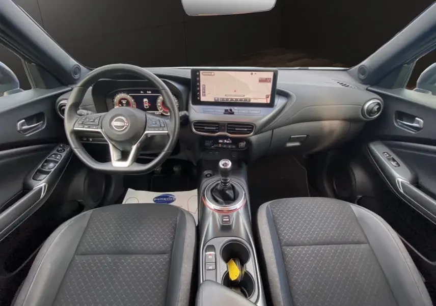Vue intérieure avant du Nissan Juke 2025 avec tableau de bord noir, écran tactile central et volant multifonctions.