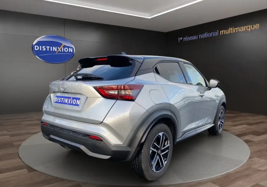 Nissan Juke gris clair vue 3/4 arrière droit, avec jantes alliage et toit noir contrasté en showroom.