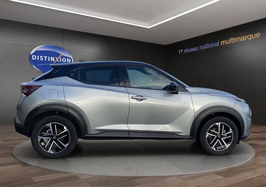 Profil droit du Nissan Juke gris clair 2025 avec jantes alliage et toit noir contrasté en showroom.
