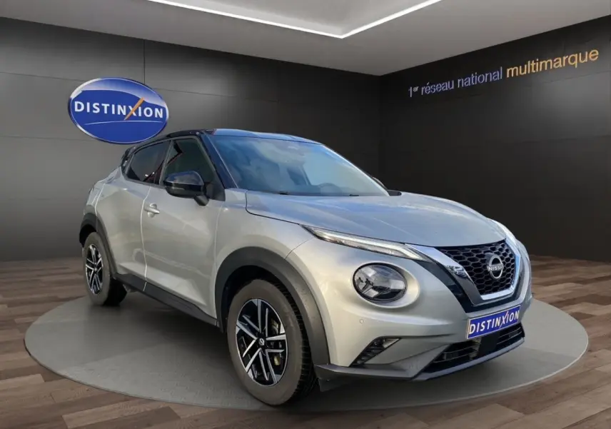 Nissan Juke gris clair vu en 3/4 avant droit, avec toit noir et jantes alliage distinctives.