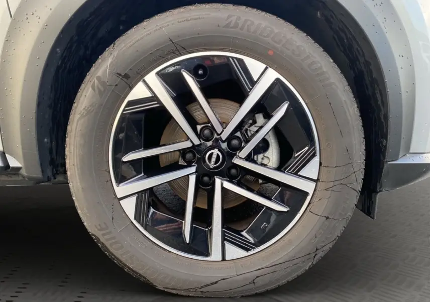 Gros plan sur la roue avant droite du Nissan Juke gris clair, mettant en valeur la jante alliage noire et argentée.