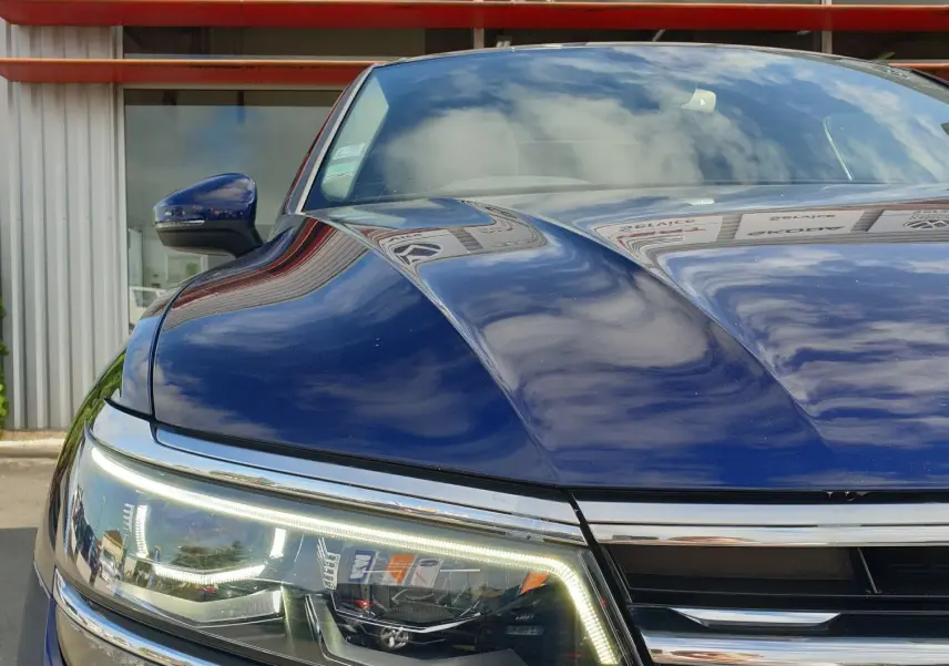 Gros plan sur l'avant gauche d'un Volkswagen Tiguan bleu Atlantique métallisé avec badge R-Line et phares LED allumés.