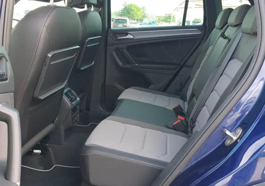 Vue intérieure côté arrière gauche du Volkswagen Tiguan bleu Atlantique, montrant les sièges arrière et le toit ouvrant panoramique.