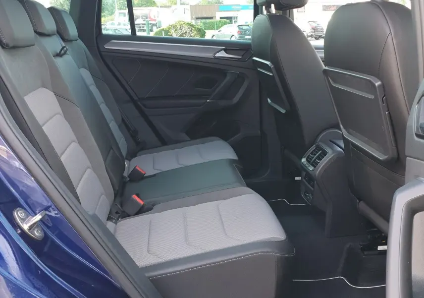 Vue intérieure arrière droite du Volkswagen Tiguan bleu Atlantique, montrant les sièges arrière et le toit ouvrant panoramique.