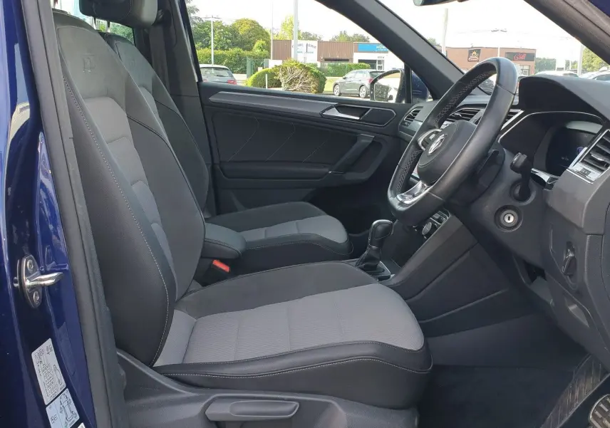 Vue intérieure côté conducteur d'un Volkswagen Tiguan bleu Atlantique avec sièges gris et volant à droite.