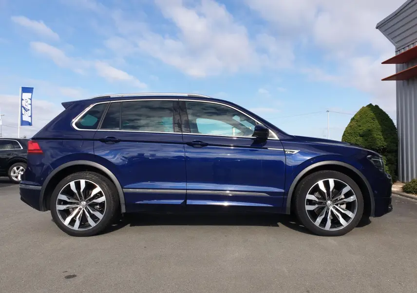 Profil droit d'un Volkswagen Tiguan bleu Atlantique métallisé avec jantes alliage et toit ouvrant visible.