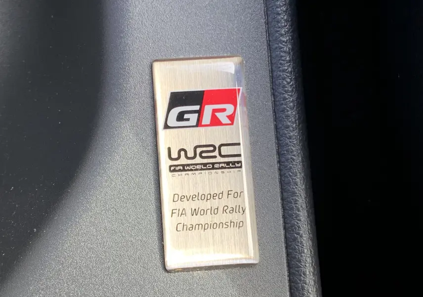 Plaque intérieure GR WRC en métal brossé sur fond noir, soulignant la version sportive Toyota Yaris 1.6 VVT-I 261 Premium.