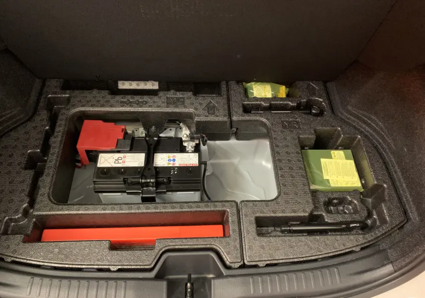 Batterie et rangement sous le coffre d'une Toyota Yaris blanche, vue en plongée sur l'espace de stockage organisé.
