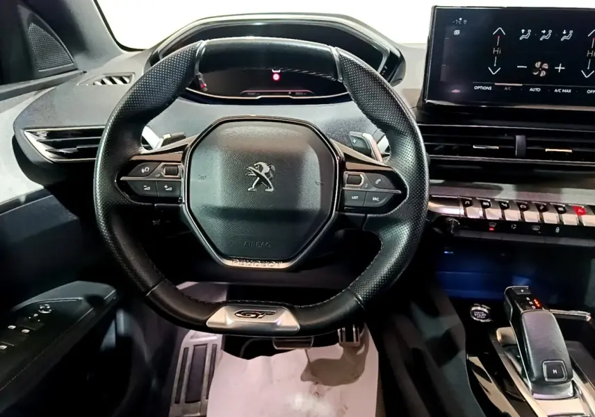 Vue intérieure centrée sur le volant cuir multifonctions noir du Peugeot 3008 GT avec tableau de bord numérique et écran tactile.