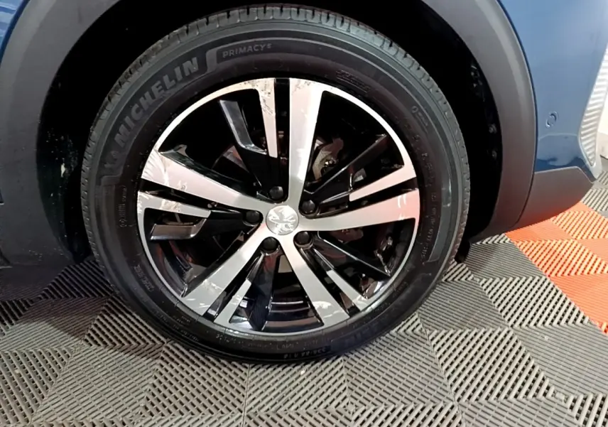 Gros plan sur la roue avant droite du Peugeot 3008 bleu, avec jante alliage bicolore et pneu Michelin.