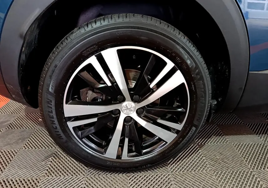 Gros plan sur la roue avant droite d’un Peugeot 3008 bleu avec jante alliage bicolore et pneu Michelin.