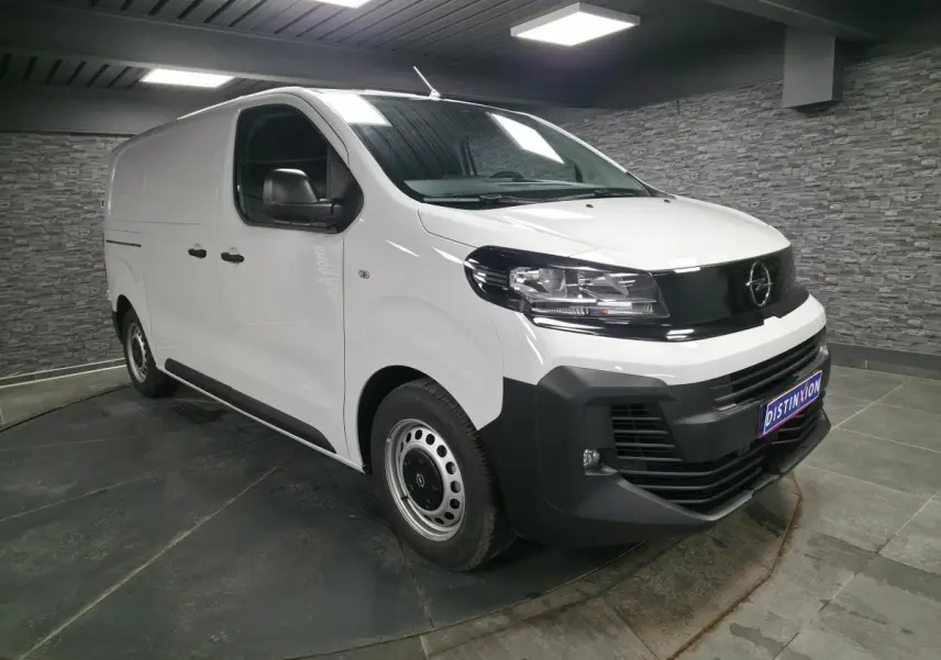 Opel Vivaro blanc en 3/4 avant droit, avec pare-chocs noirs et jantes tôles grises, en intérieur showroom.