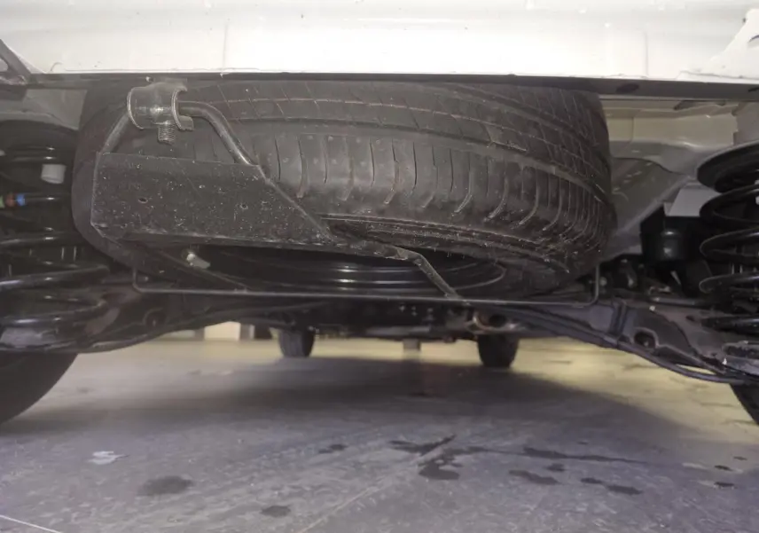 Vue en contre-plongée sous l'arrière d'un Opel Vivaro blanc, montrant la roue de secours et la suspension.