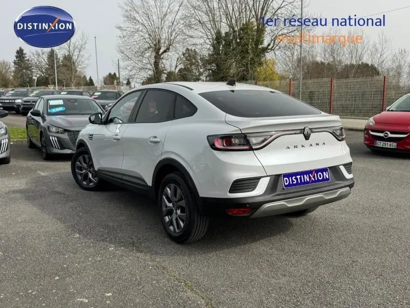 Vue 3/4 arrière droite d'un Renault Arkana blanc 2025 avec feux arrière reliés et logo distinctif sur parking.
