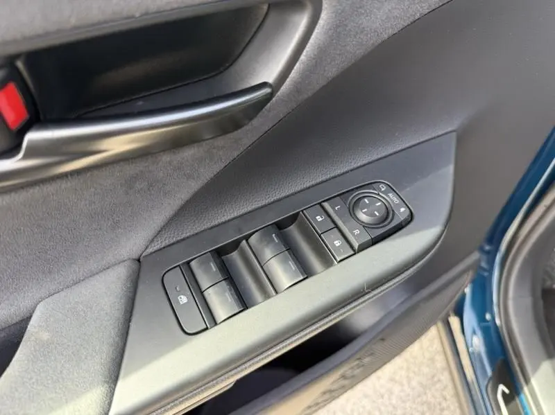 Gros plan sur la commande des vitres et rétroviseurs côté gauche d’un Toyota C-HR Hybride bleu persan 2024.