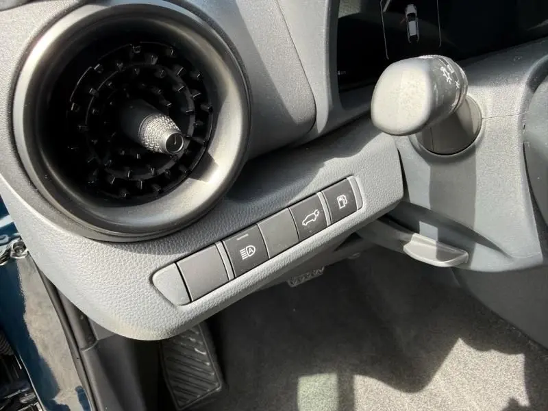 Détail intérieur côté gauche du tableau de bord du Toyota C-HR Hybride 2024, avec commandes d’éclairage et ouverture du coffre.