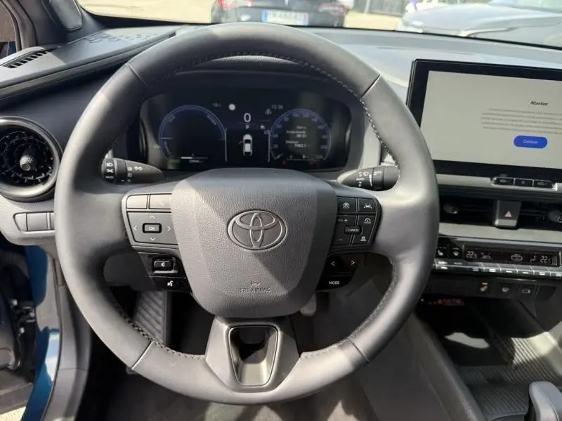Vue intérieure centrée sur le volant du Toyota C-HR Hybride bleu persan 2024, avec tableau de bord numérique et écran tactile.