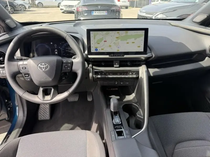 Vue intérieure du tableau de bord et volant du Toyota C-HR Hybride 2024 bleu persan avec écran tactile central et console moderne.