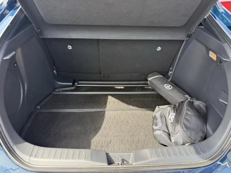 Coffre ouvert d’un Toyota C-HR Hybride bleu persan 2024, avec tapis de coffre et sac Toyota noir visible.