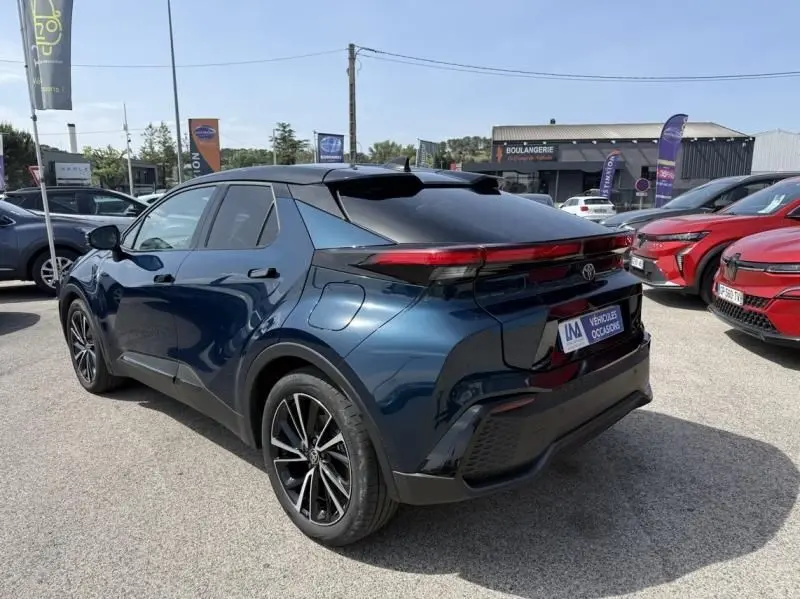 Vue 3/4 arrière droite d'un Toyota C-HR Hybride 2024 bleu persan avec toit noir et feux arrière fins reliés.