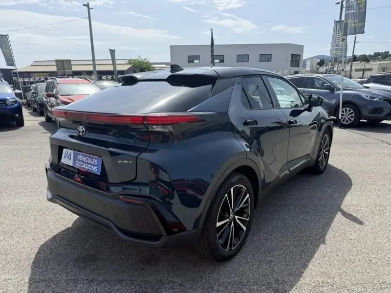 Vue 3/4 arrière droite du Toyota C-HR Hybride 2024 en bleu persan, avec feux arrière fins et jantes noires distinctives.