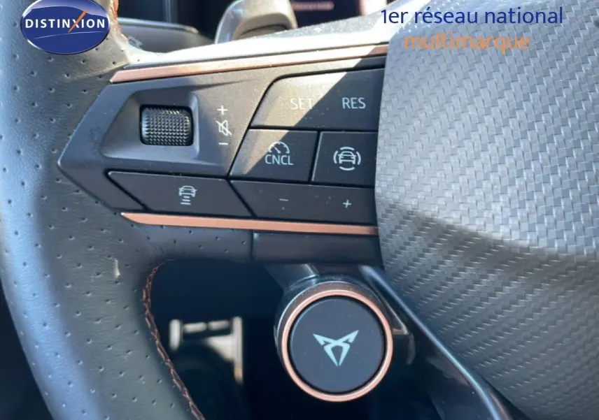 Gros plan sur le volant en cuir perforé avec commandes multifonctions et logo CUPRA au centre, intérieur noir.