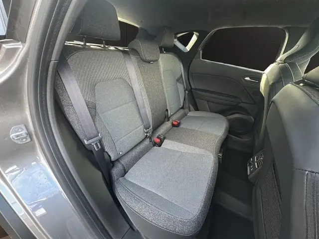 Vue intérieure côté arrière gauche du Renault Captur gris foncé 2025, montrant la banquette arrière en tissu gris avec ceintures de sécurité.