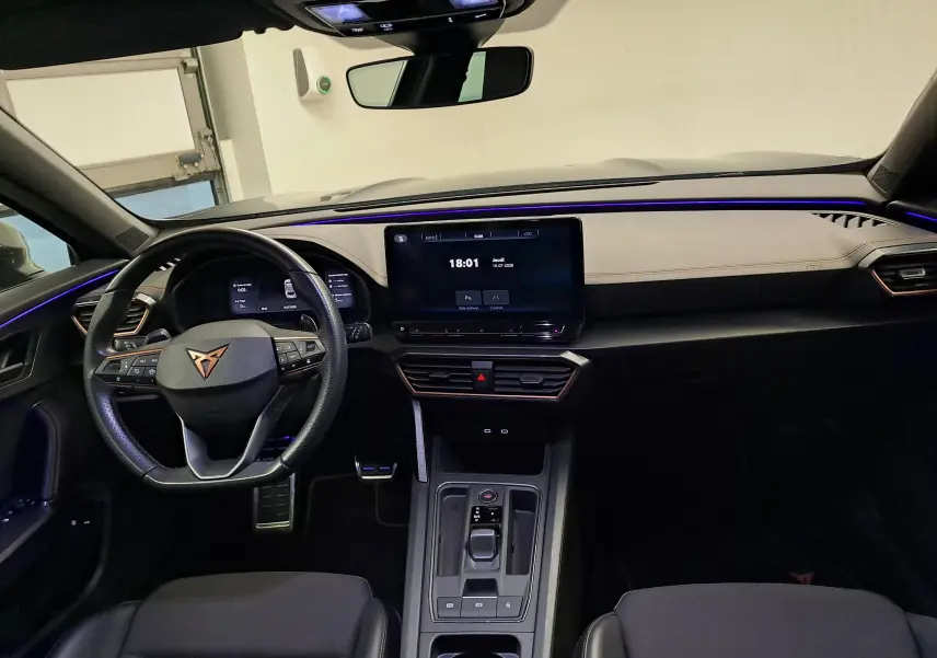 Vue intérieure frontale du CUPRA Formentor 1.4 e-HYBRID 245 DSG6 VZ avec tableau de bord clair et éclairage d’ambiance violet.