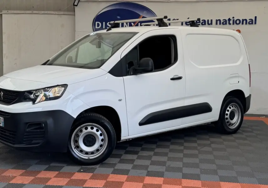 Vue 3/4 avant droit d'un utilitaire Peugeot Partner blanc avec barres de toit et jantes acier grises.