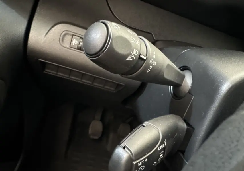 Gros plan sur les commandes de phares et régulateur de vitesse dans l'habitacle noir du Peugeot Partner 2021.