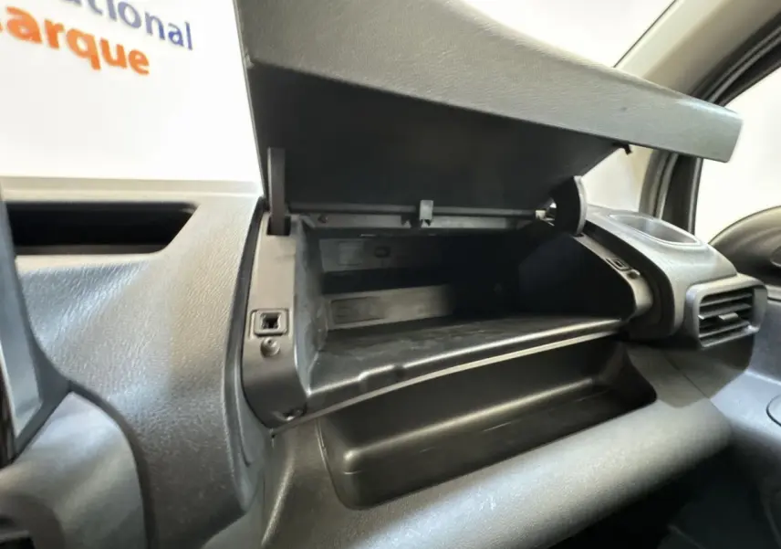 Gros plan sur la boîte à gants ouverte côté passager dans l’habitacle noir du Peugeot Partner blanc.