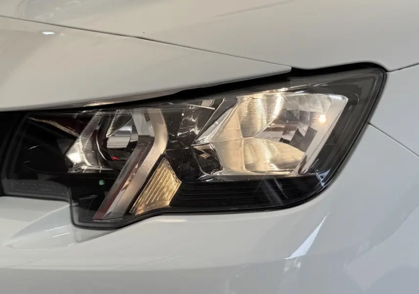 Gros plan sur le phare avant droit du Peugeot Partner blanc, mettant en valeur son design moderne et précis.