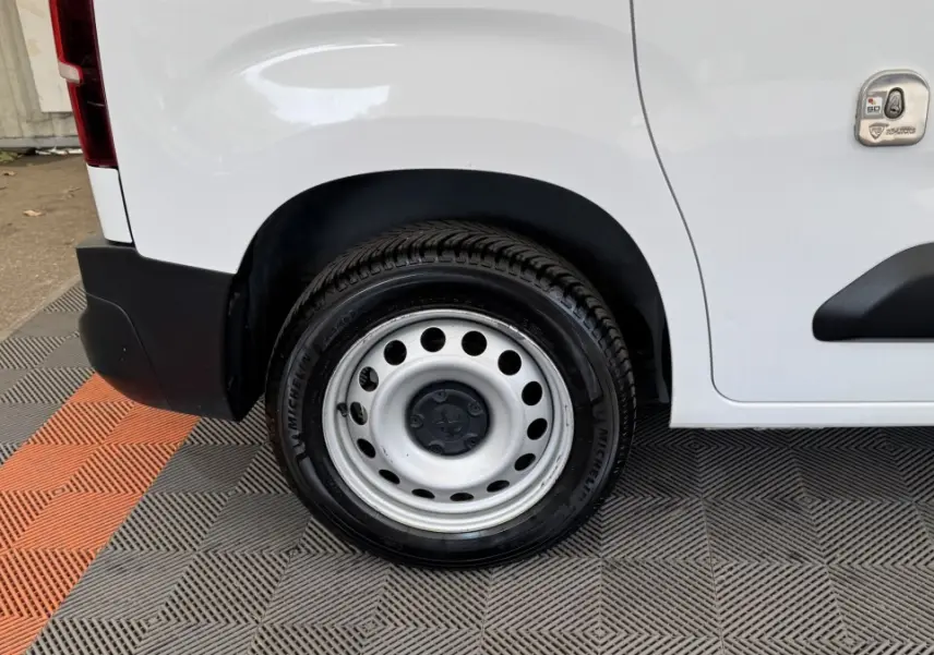 Gros plan sur la roue arrière droite acier d’un Peugeot Partner blanc avec pare-chocs noir et trappe latérale.