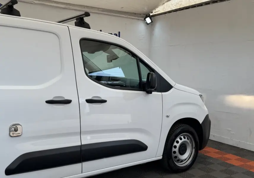 Vue de profil côté droit du Peugeot Partner blanc utilitaire avec protections noires et toit équipé de barres.