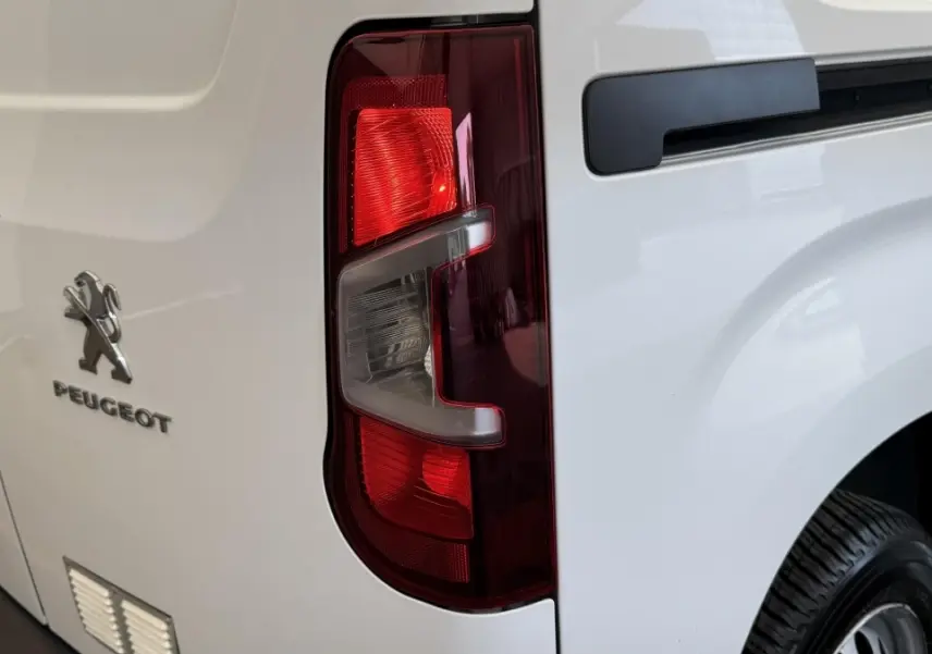 Gros plan sur le feu arrière droit d’un Peugeot Partner blanc, avec logo et partie de la porte arrière visible.