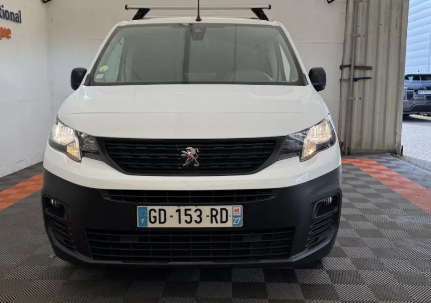 Vue de face du Peugeot Partner blanc avec calandre noire et phares allumés dans un garage.