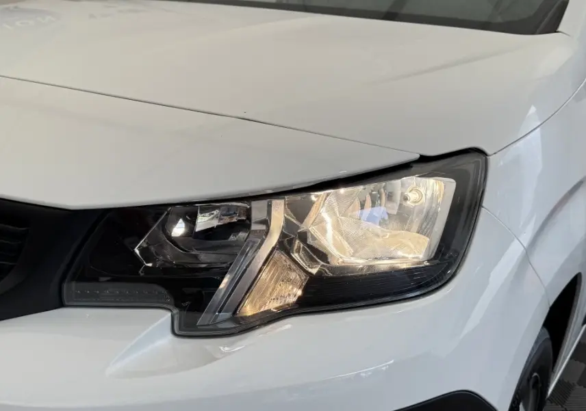 Gros plan sur le phare avant droit du Peugeot Partner blanc, mettant en valeur les détails du bloc optique.