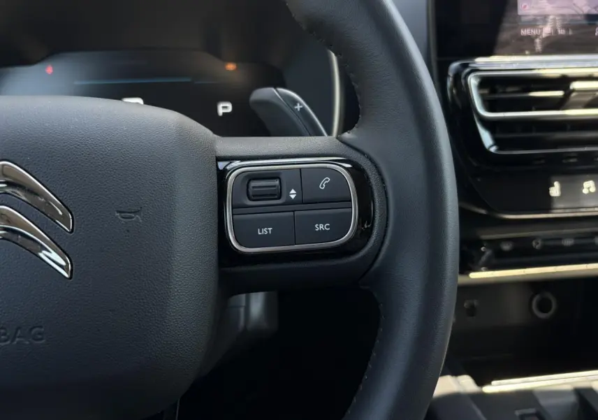 Gros plan sur le volant en cuir noir du Citroën C5 Aircross Hybrid 2025, avec commandes intégrées et tableau de bord partiel.