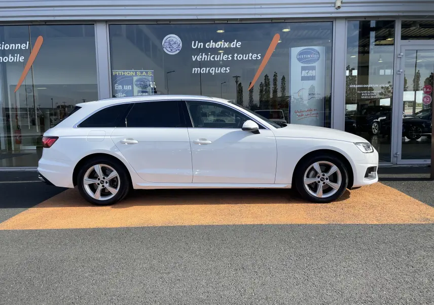 Audi A4 Avant blanc vue de profil côté gauche, garée devant une vitrine de concession multimarque.