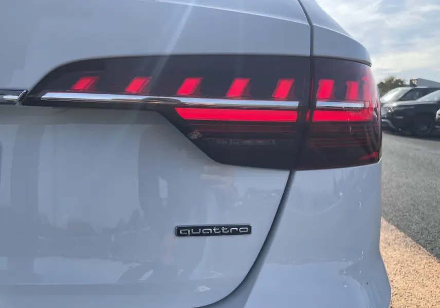 Gros plan sur le feu arrière droit rouge et blanc d'une Audi A4 Avant 40 TDI blanc avec logo quattro sur la malle arrière.