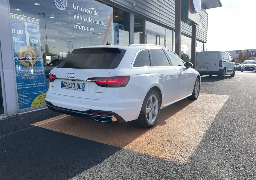 Audi A4 Avant blanc vue 3/4 arrière droit stationnée devant un showroom avec vitres teintées et feux LED allumés.