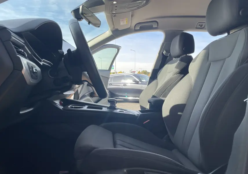 Vue intérieure côté conducteur de l'Audi A4 Avant 40 TDI 204 Quattro 2022 avec sièges tissu gris noir et tableau de bord moderne.