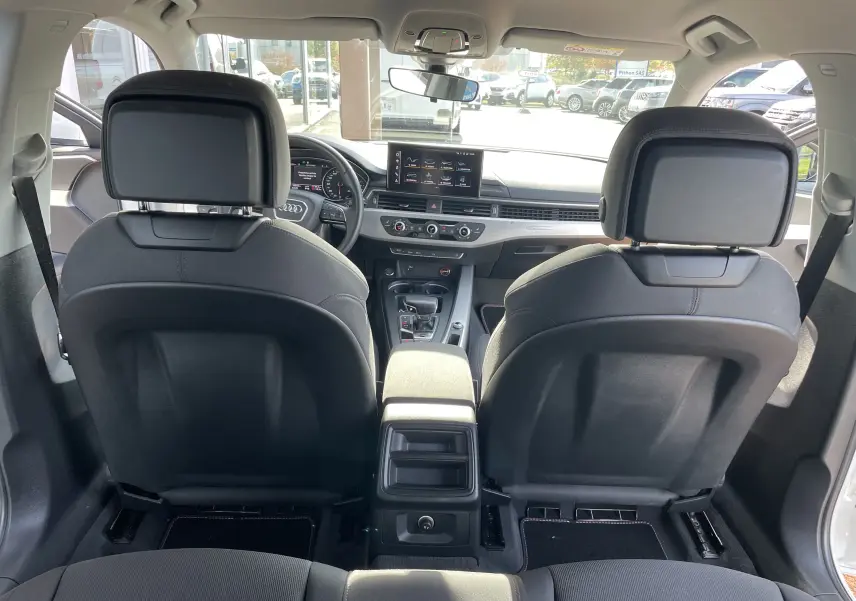 Vue depuis la banquette arrière de l'habitacle gris noir d'une Audi A4 Avant 40 TDI blanc, avec tableau de bord et écran central visibles.