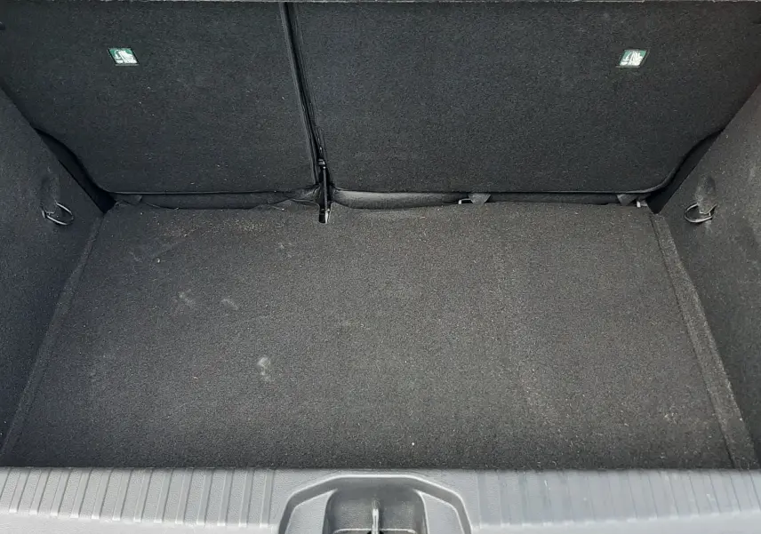 Coffre vide vu de dessus de la Renault Clio V gris titanium, montrant la moquette noire et les dossiers arrière rabattus.