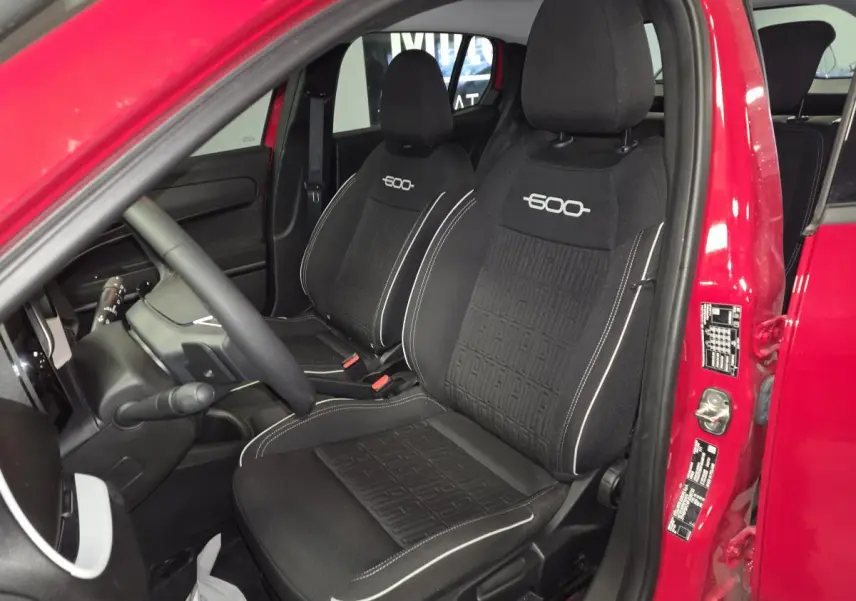 Intérieur côté conducteur d'une FIAT 600 rouge 2024, sièges noirs avec logo 600 brodé et tableau de bord visible.